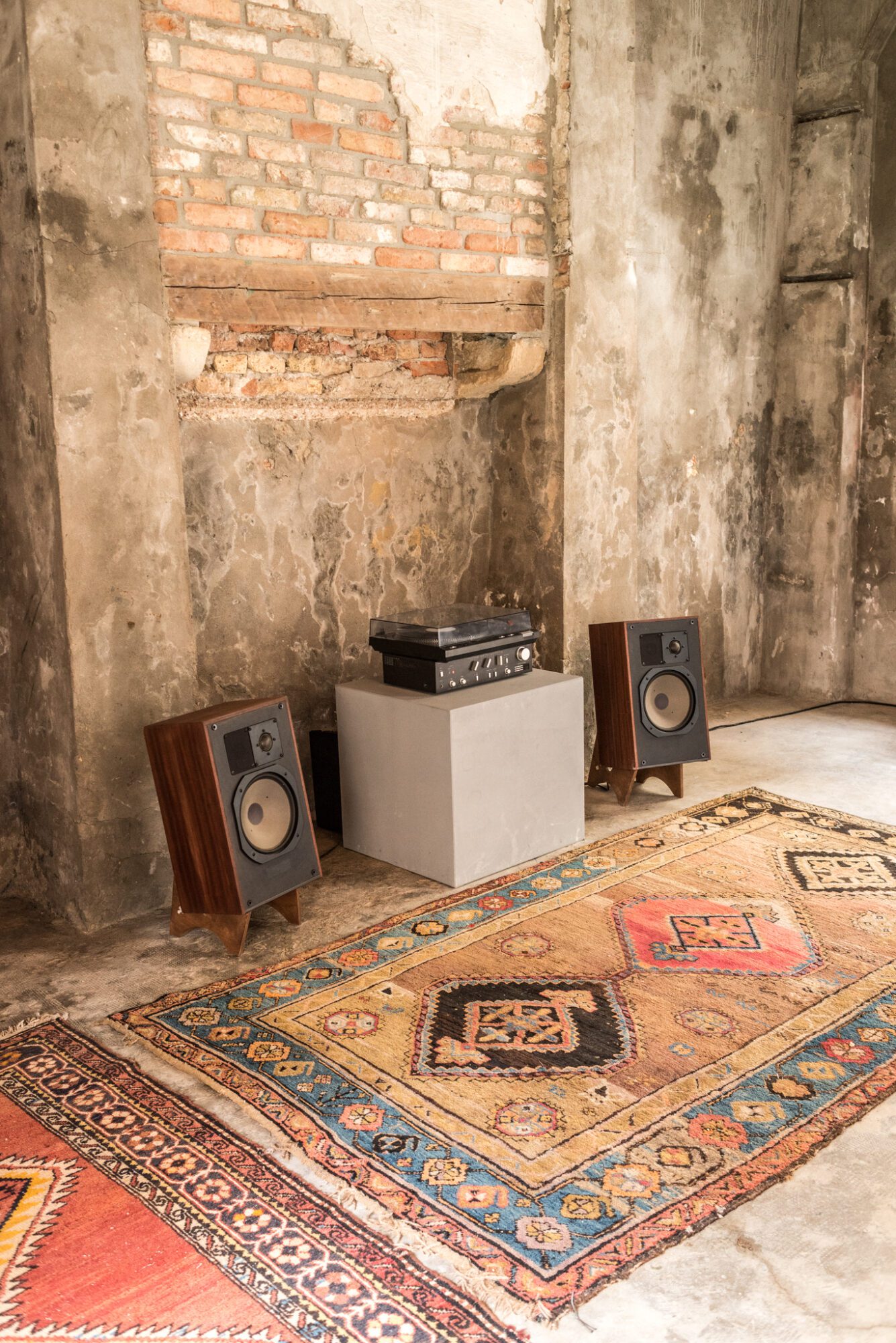 An installation view of Andrius Arutiunian piece with two speakers, a vinyl player, and carpets at Venice Biennale