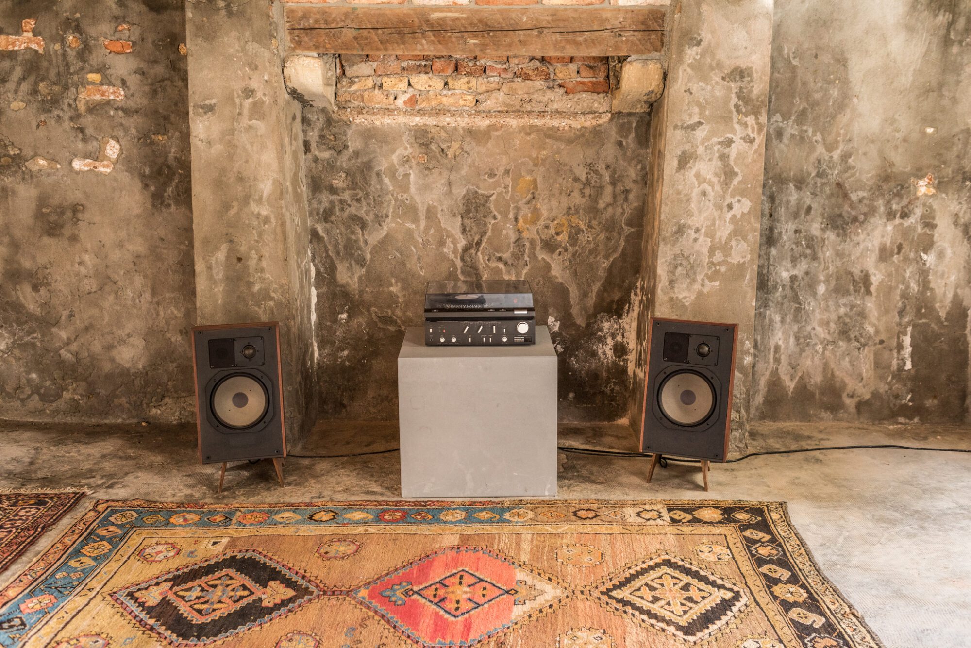 An installation view of Andrius Arutiunian piece with two speakers, a vinyl player, and carpets at Venice Biennale